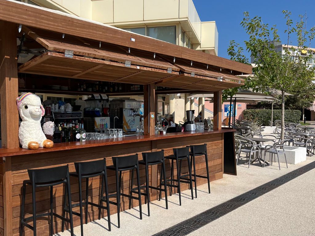 An outdoor bar area with a wooden counter, black bar stools, and a large stuffed llama decoration.