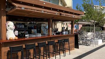 An outdoor bar area with a wooden counter, black bar stools, and a large stuffed llama decoration.