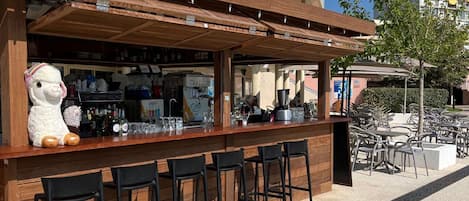 An outdoor bar area with a wooden counter, black bar stools, and a large stuffed llama decoration.
