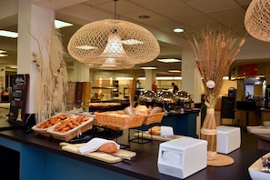 Un buffet proposant une variété de plats, notamment du pain et des pâtisseries, dans un espace intérieur bien éclairé, agrémenté de luminaires suspendus.