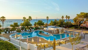 Área da piscina com espreguiçadeiras e guarda-sóis, com vista para uma praia e o mar.