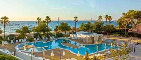 A pool area with lounge chairs and umbrellas, overlooking a beach and the sea.
