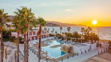 Ein Resort mit Pool, Palmen und Blick auf den Ozean bei Sonnenuntergang.