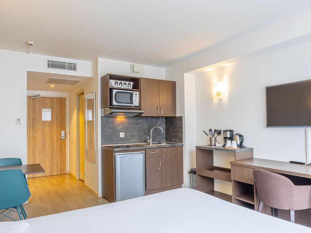 Habitación de hotel compacta con kitchenette, cama, escritorio y televisor.