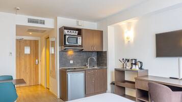Habitación de hotel compacta con kitchenette, cama, escritorio y televisor.