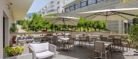 An outdoor patio with wicker furniture, umbrellas, and potted plants.