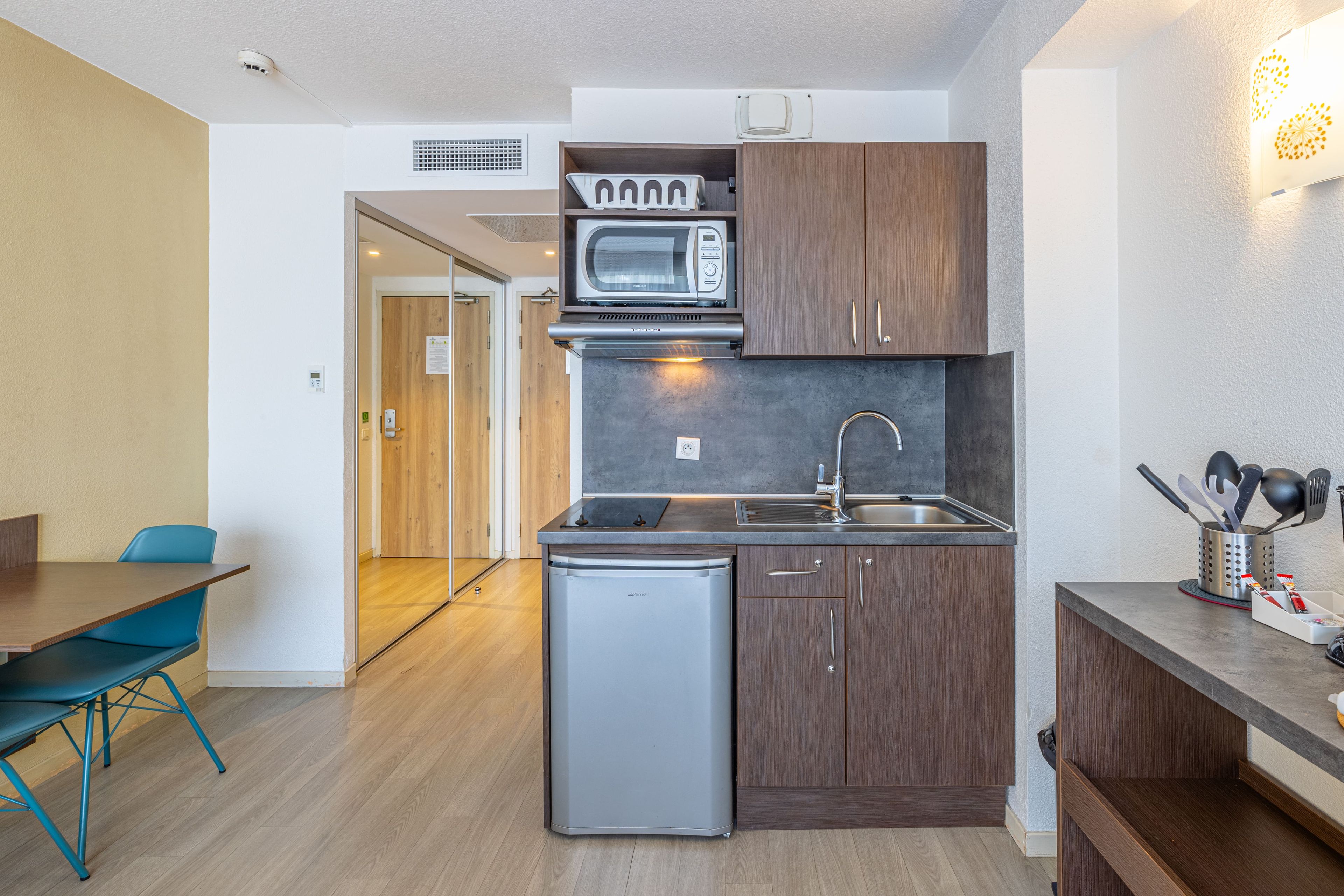 Cocina compacta con microondas, pileta y heladera pequeña. Hay un comedor con mesa y sillas.