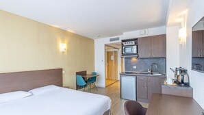 A hotel room with a bed, a desk, a microwave, and a small kitchenette. - Studio tout confort au coeur d'Aix-les-Bains (Aix-les-Bains)