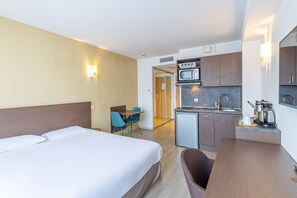 Een hotelkamer met een bed, een bureau, een magnetron en een kleine keukenhoek.