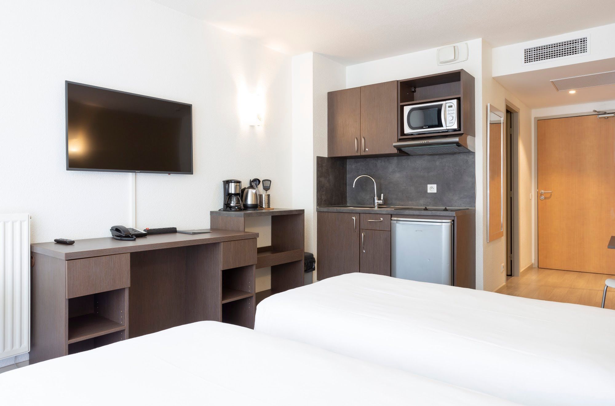 Een hotelkamer met een bed, een bureau, een flatscreen televisie, een kitchenette met een magnetron en een spoelbak.