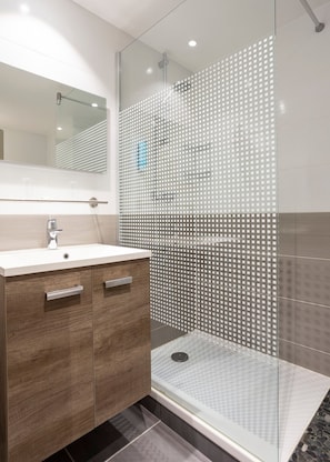 Een moderne badkamer met een glazen douchecabine, een houten wastafelmeubel en een grote spiegel.