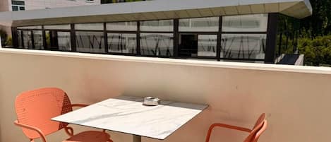 En terrasse med to orange stole og et bord, med udsigt til en bygning mod en bjergkulisse.