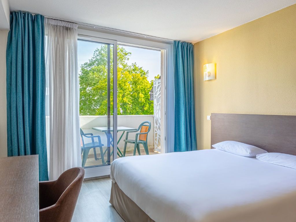 Een hotelkamer met een bed, een bureau en uitzicht op de omgeving door een schuifdeur.