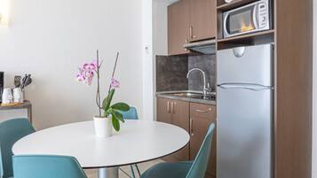 Une cuisine moderne équipée d’un réfrigérateur, d’un four à micro-ondes et d’un évier en acier inoxydable. On y trouve une table ronde avec des chaises et une plante en pot, une orchidée.