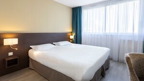 Une chambre d’hôtel avec un lit, des lampes de chevet, une fenêtre avec des rideaux et une chaise.