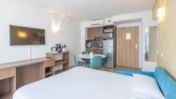 Une chambre d’hôtel comprenant un lit, un bureau, une table à manger avec des chaises, un coin cuisine et un téléviseur.