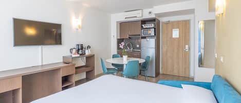 Et hotelværelse med seng, skrivebord, spisebord med stole, et tekøkken og et fjernsyn.