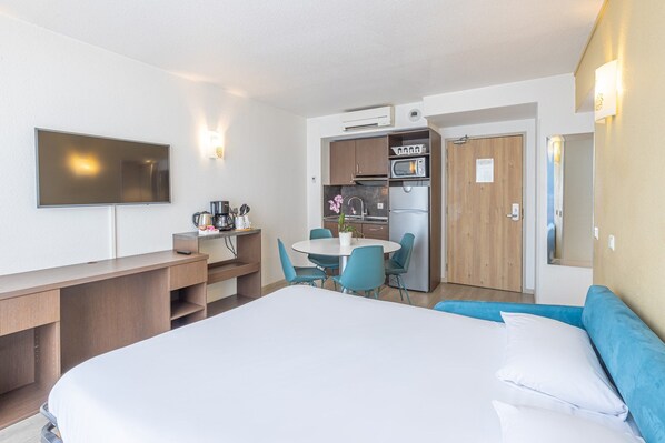 Habitación de hotel con cama, escritorio, mesa de comedor con sillas, kitchenette y televisor.