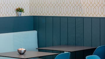 Een restaurantinterieur met een patroonmuur, een blauwe gestoffeerde bank en een tafel met een kom eten.