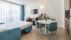 Habitación de hotel con cama, escritorio, mesa de comedor con sillas, televisor montado en la pared y zona de cocina.