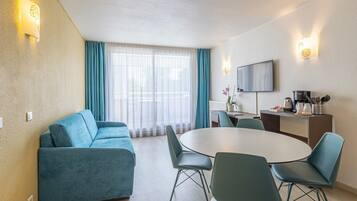 Ein modernes Hotelzimmer mit einer Couch, einem Esstisch, Stühlen, einem Flachbildfernseher und einer Küchenzeile.