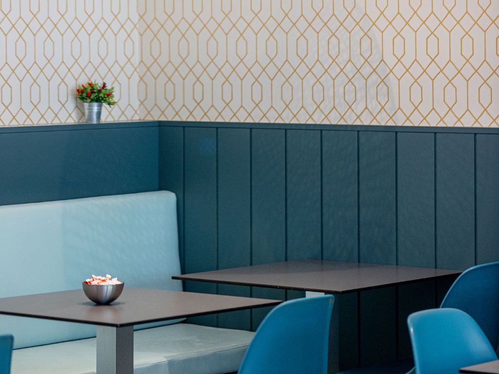 L’intérieur d’un restaurant, avec un mur orné de motifs, un banc bleu rembourré et une table sur laquelle se trouve un bol de nourriture.