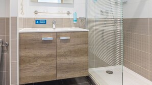 Un baño moderno con tocador de madera, cabina de ducha de vidrio y un cartel visible que indica la conservación del agua.