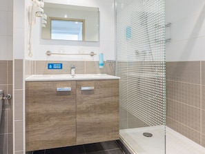 Un baño moderno con tocador de madera, cabina de ducha de vidrio y un cartel visible que indica la conservación del agua.