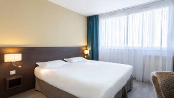 Een hotelkamer met een bed, nachtlampjes, een nachtkastje, een stoel en een raam met gordijnen.