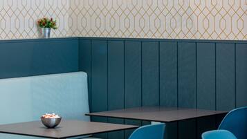 L’intérieur d’un restaurant, avec un mur orné de motifs, un banc bleu rembourré et une table sur laquelle se trouve un bol de nourriture.