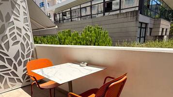 Un balcon avec deux chaises et une table, donnant sur un immeuble doté de grandes fenêtres et de verdure.