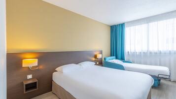 Une chambre d’hôtel avec deux lits, une table de chevet, une lampe fixée au mur et une fenêtre avec des rideaux.