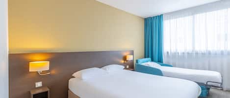 Habitación de hotel con dos camas, una mesita de noche, una lámpara de pared y una ventana con cortinas.