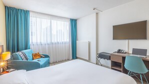 Una camera d'albergo con un letto, una scrivania con un computer, una sedia, una televisione e una finestra con tende.