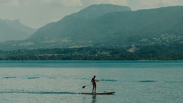 Une personne fait de la planche à pagaie sur une étendue d'eau calme, avec des montagnes en arrière-plan.
