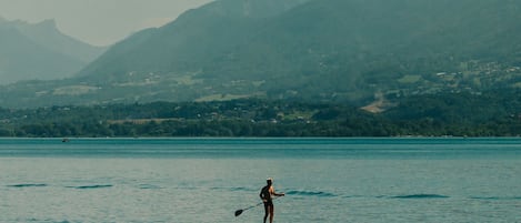 En person står på paddleboard på et roligt vandareal med bjerge i baggrunden.