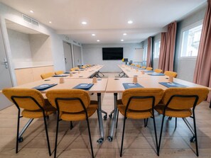A conference room with a long table, yellow chairs, and a large screen at the front.