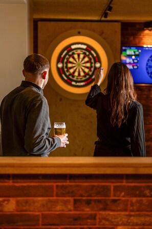 Two people standing in front of a dartboard with a television screen in the background.