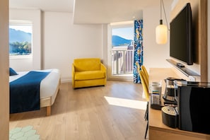 Una camera d'albergo con un letto, una poltrona gialla, una televisione e una macchina per il caffè.