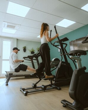A gym with stationary bikes and a treadmill, a man using the treadmill, and a woman on a stationary bike.
