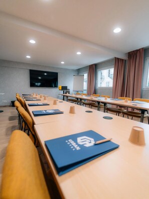 A conference room with multiple tables, chairs, a projector screen, and a television.