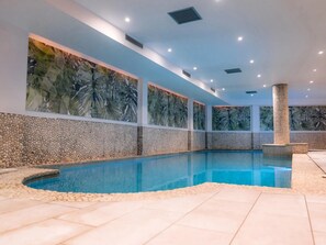 A swimming pool with a pebble-lined edge, surrounded by walls with a tropical leaf pattern.