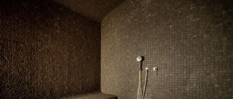 A dimly lit, tiled room with a bench and a shower area.