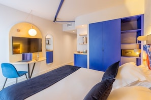 Una camera d'albergo moderna con un letto, una scrivania, una TV, uno specchio e un armadio.