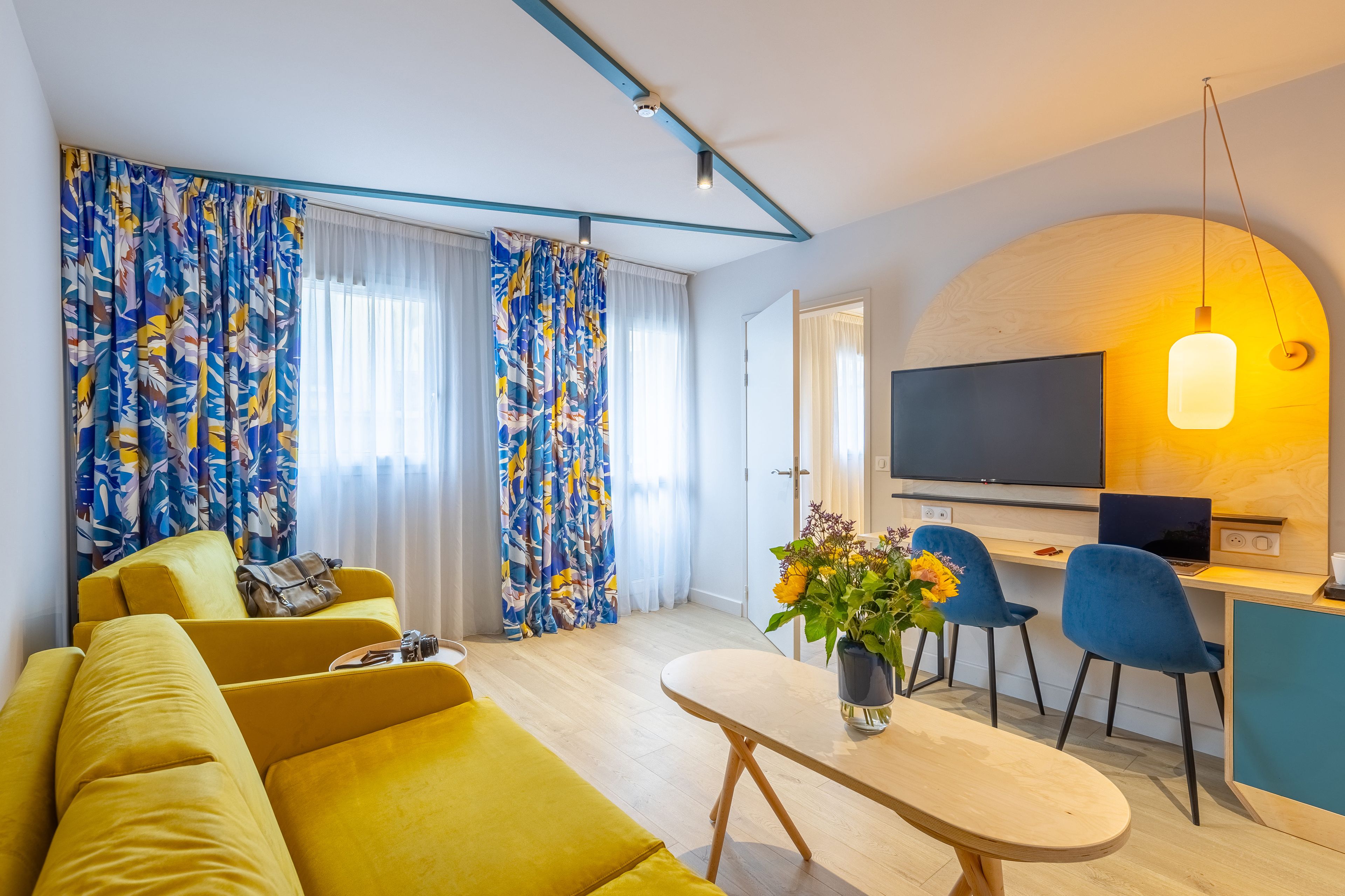 Een moderne woonkamer met een bank, een eethoek met stoelen, een televisie en een tafel met een bloevas.