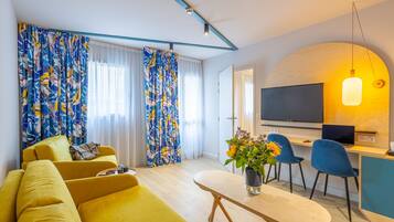 Een moderne woonkamer met een bank, een eethoek met stoelen, een televisie en een tafel met een bloevas.