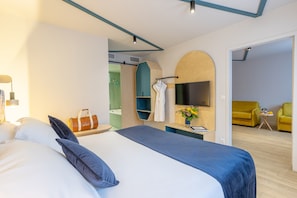 Een moderne hotelkamer met een groot bed, een televisie, een badkamer met douche en een zithoek met een gele bank.
