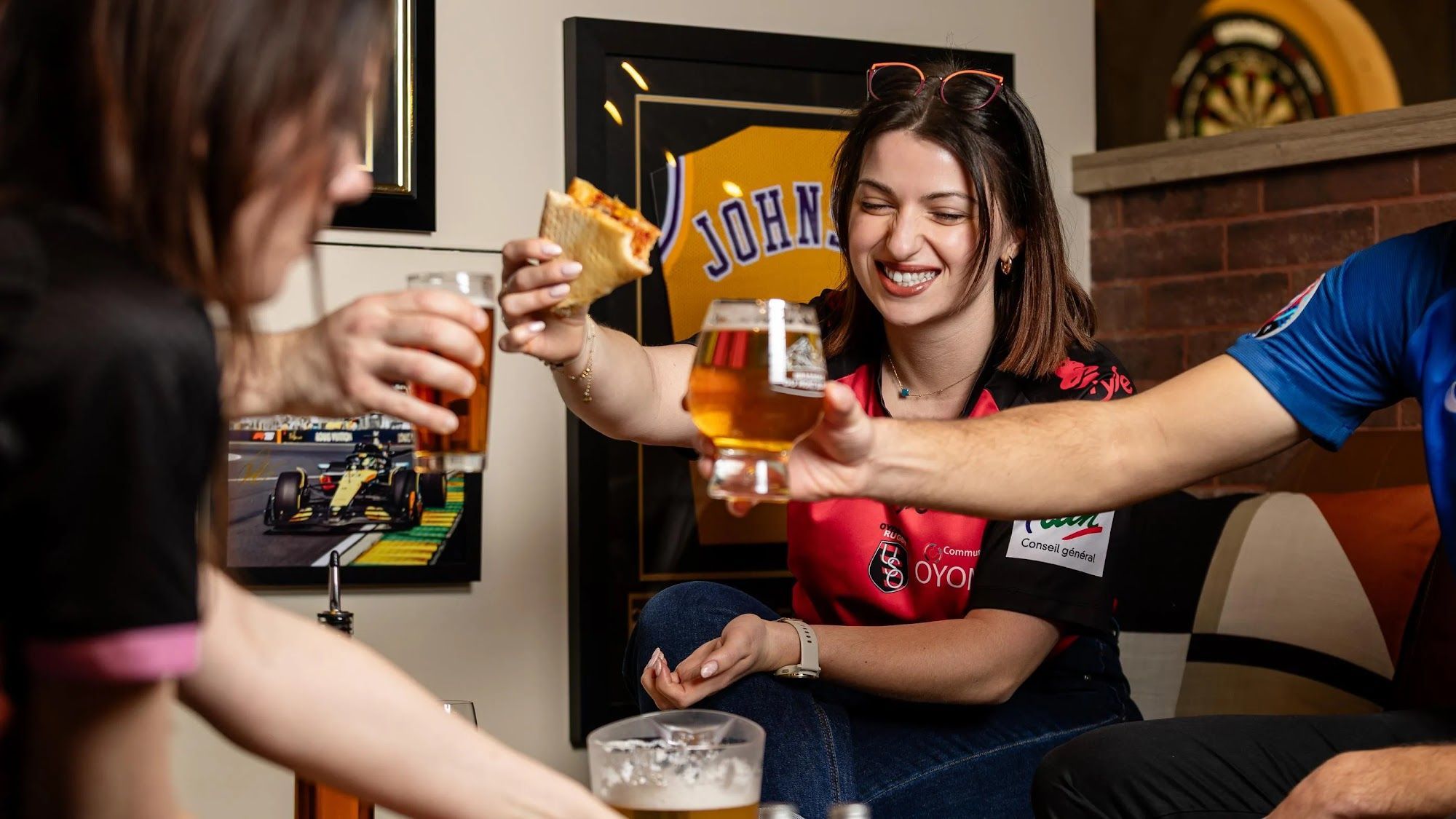 Iemand houdt een glas bier en een plak pizza vast.