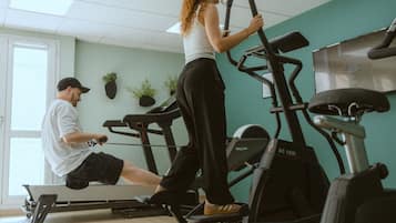 Une salle de sport équipée de vélos d’appartement et d’un tapis de course, un homme qui utilise le tapis de course et une femme sur un vélo d’appartement.