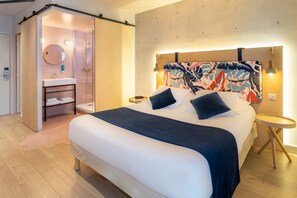 Una camera d'hotel moderna con un letto grande, una zona doccia e un pavimento in legno.